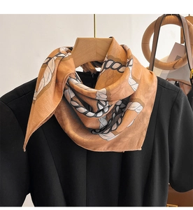 Close-up of silk scarf with orange chain pattern tied on a black top on wooden hanger