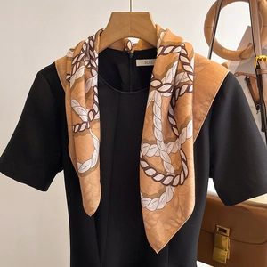Caramel silk scarf with chain print draped elegantly on a black dress in interior setting