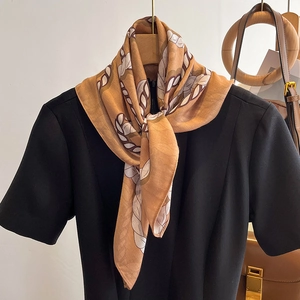 Elegant chain print silk scarf in ginger yellow styled on a black top with accessories