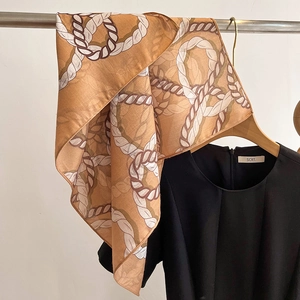 Detail of golden chain pattern silk scarf hanging on a wooden hanger with black top