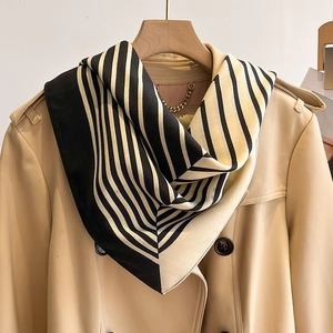 Detailed texture of black and beige striped silk scarf paired with a trench coat