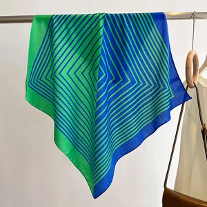 Detail of a geometric striped square scarf in green and blue hanging on a metal rod