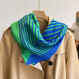 Detail of striped silk-feel scarf in green and blue styled on a beige trench coat