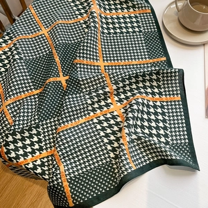 Détail d'une écharpe pied-de-poule avec lignes orange sur un bureau blanc