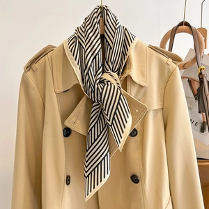 Detail eines schwarz-weiß gestreiften Schals an einem beigen Trenchcoat-Revers