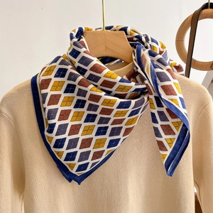Elegant diamond pattern silk scarf in navy and yellow draped over a sweater on a wooden hanger