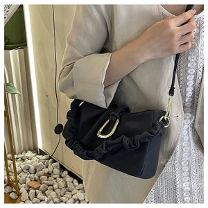 Detail of pleated black shoulder bag with gold D-ring hardware on a stylish model