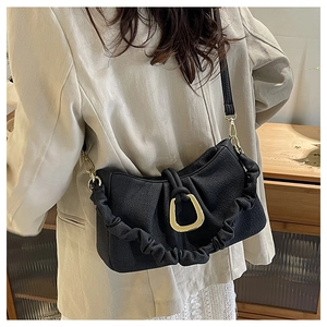 Detail of black pleated crossbody bag featuring a large golden horseshoe buckle on leather