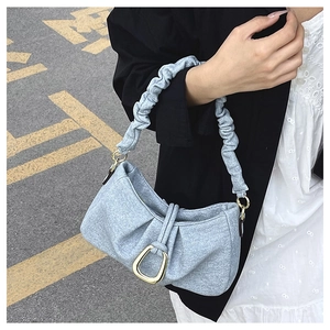 Detail of light blue textured fabric shoulder bag with pleated strap and gold buckle