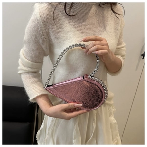 Detail of a pink metallic heart-shaped handbag with a crystal-encrusted handle on white dress