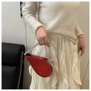 Detail of red heart-shaped evening clutch with sparkling rhinestone handle and metallic finish
