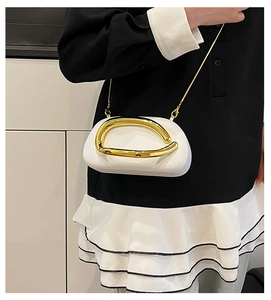 Detailed view of white minimalist handbag with gold curved handle and chain strap