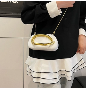 Detail of white semi-round bag featuring distinctive gold arc metal handle and chain