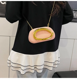 Detail view of pink crossbody bag featuring a large polished gold C-shaped metal ornament