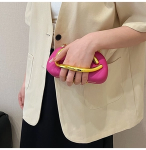 Detail of fuchsia evening clutch bag featuring a prominent gold circular metal handle
