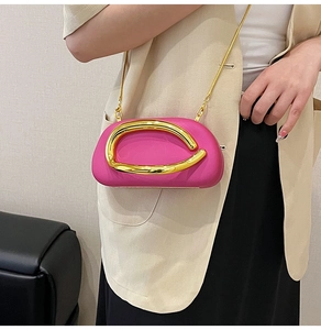 Detail of fuchsia clutch bag with gold chain and artistic metal ring on neutral suit