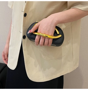 Detail of black matte evening clutch with gold metal curved handle on a beige suit outfit