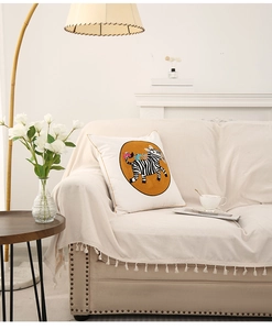Detail of beige sofa throw with fringe and white cartoon zebra pillow in a cozy living room