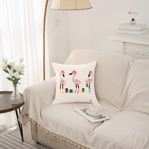 Square cream pillow cover with festive flamingo print on a sofa in a modern room