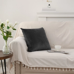Cuscino in velluto grigio scuro su copridivano beige con frange in un ambiente elegante