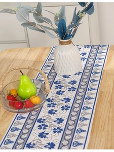 Close-up of modern floral table runner with blue tassels on a rustic wooden dining table