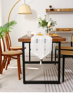 Close-up of white woven table runner with geometric texture and tassel on wooden table