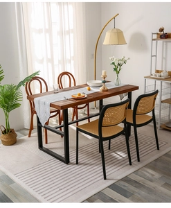 Detail of a solid wood dining table with black U-shaped metal frame and woven rattan chairs