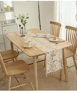 Close-up of vintage floral lace table runner with fringe tassels on a wooden dining table