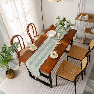 Green woven table runner with white geometric waves and tassel fringe on wood table