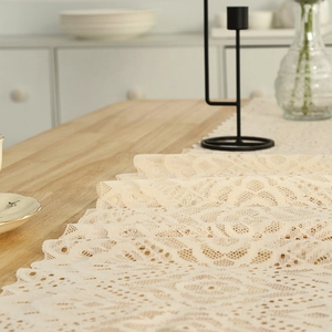 Vintage cream lace table runner with hollowed-out floral pattern on a wood table
