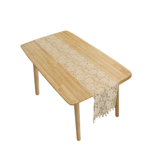 Vintage beige floral lace table runner with tassels on a wooden dining table