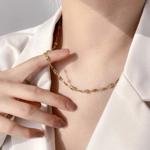 Minimalist gold coffee bean link chain necklace worn on a model in a white blazer