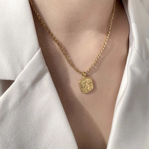 Gros plan d'un collier à pendentif rectangulaire fleuri doré sur un blazer blanc