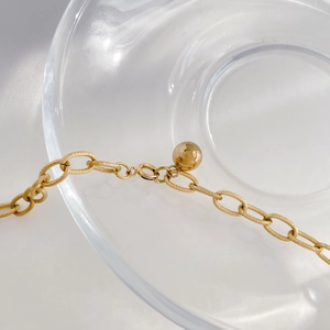 Detailed close-up of golden pig nose link necklace with textured finish and sphere charm