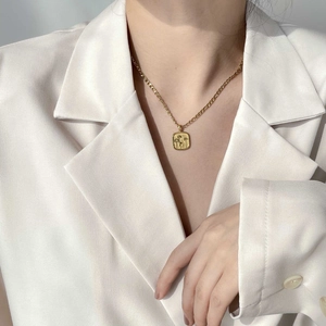 Collier à pendentif carré doré avec gravure florale porté sur un blazer blanc