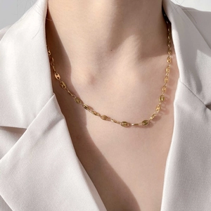 Close-up of a gold pig nose chain necklace styled with a minimalist white suit jacket