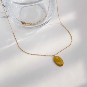 Détail d'un collier en or avec pendentif ovale gravé de motifs floraux sur fond blanc