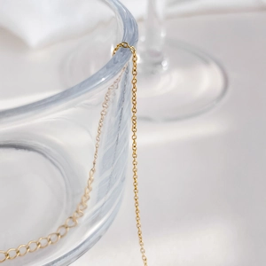 Détail d'un collier élégant à maillons dorés drapé sur un vase en verre transparent