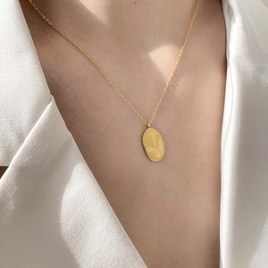 Détail d'un collier pendentif ovale en or 18 carats avec gravure florale porté par un mannequin