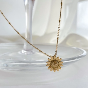 Detailaufnahme einer goldenen Sonnenblumen-Halskette mit Perlenkette auf Glasrand