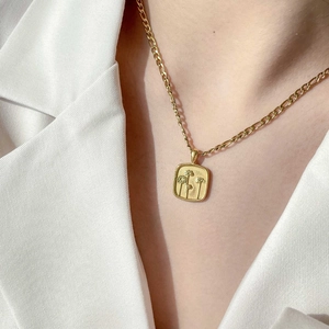 Gros plan d'un collier à pendentif floral rectangulaire doré sur blazer blanc