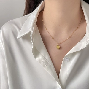 Detail einer goldenen Sonnenkette mit Perlenkette auf weißem Seidenhemd