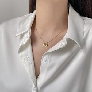 Detailansicht einer goldenen Sonnenblumen-Halskette getragen auf einer Seidenbluse