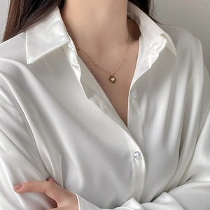 Detailansicht der Gänseblümchen-Halskette auf weißer Satinbluse mit eleganten Goldperlen