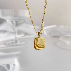 Gros plan d'un collier doré avec pendentif rectangulaire sur fond élégant texturé