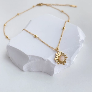 Detail der Sonnenanhänger-Halskette mit rosa Edelstein und goldener Perlenkette