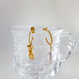 Détail de boucles d'oreilles asymétriques avec perle baroque sur un verre poli