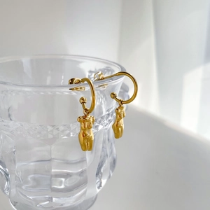 Boucles d'oreilles dorées avec pendentif buste féminin exposées sur un verre