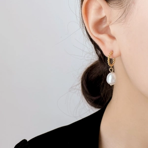 Détail de boucles d'oreilles dorées torsadées avec perle baroque sur mannequin élégant