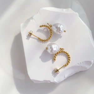 Détail de boucles d'oreilles torsadées en or avec perles baroques sur pierre blanche